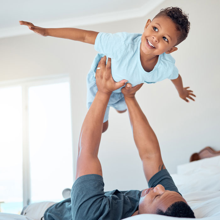 man holding smiling young boy in the air at home