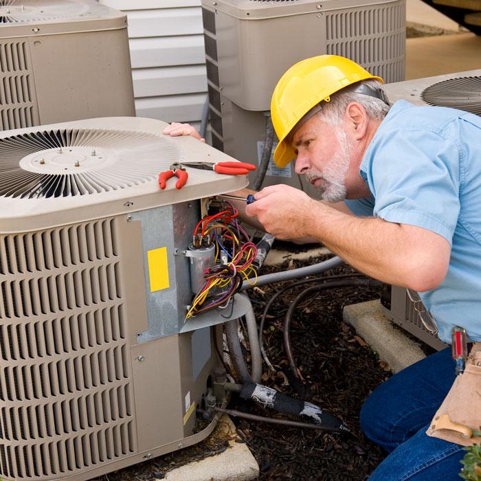 Technician in a hard hat repairing an AC unit in Volusia and Flagler Counties, FL.